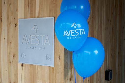 A wooden wall with a sign that says Avesta Housing and blue balloons.