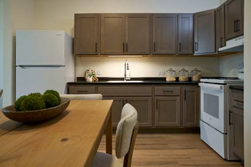 A kitchen with a wooden table and chairs, a white refrigerator, and brown cabinets.