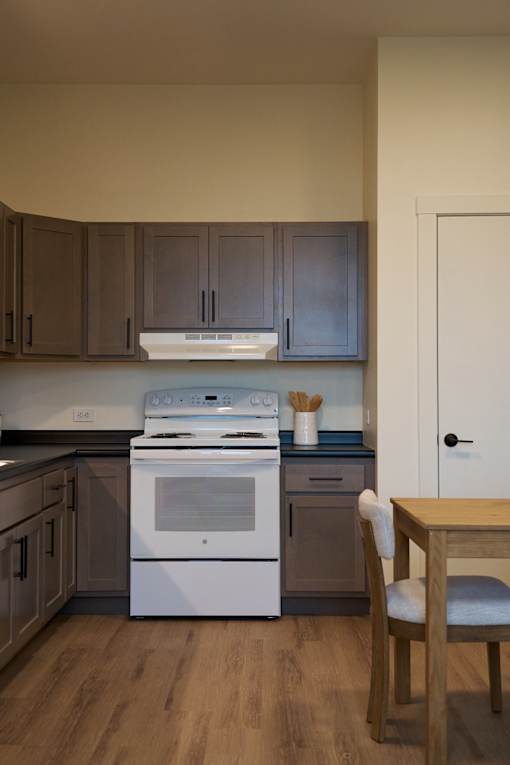A kitchen with a white stove top oven and wooden floors.