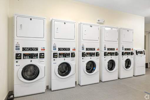 A row of white washing machines are lined up against a wall.