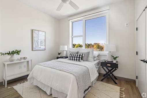 A bedroom with a large bed, a ceiling fan, and a window with a view of trees outside.