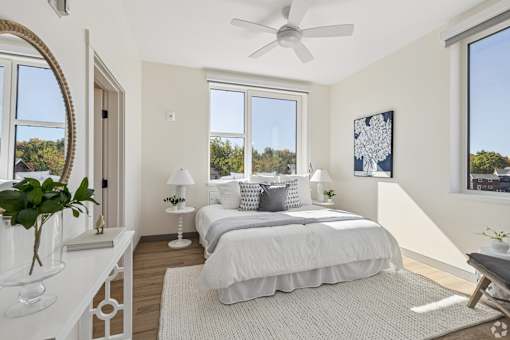 A bedroom with a large bed, a ceiling fan, and a view of trees outside the window.