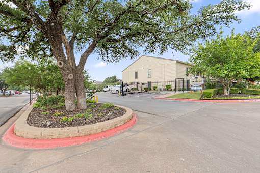 Gated property entrance with tree and landscaping at Parks on the Green Apartments, Temple, 76504
