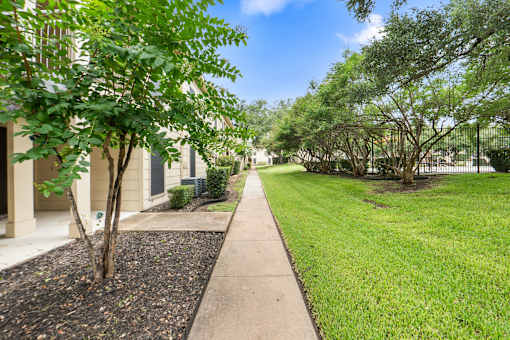 Walkway between buildings with mature trees and lawn at Parks on the Green Apartments, Temple, TX