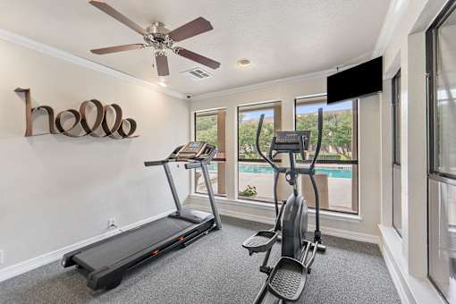 Home gym with treadmill and elliptical overlooking pool at Parks on the Green Apartments, Texas