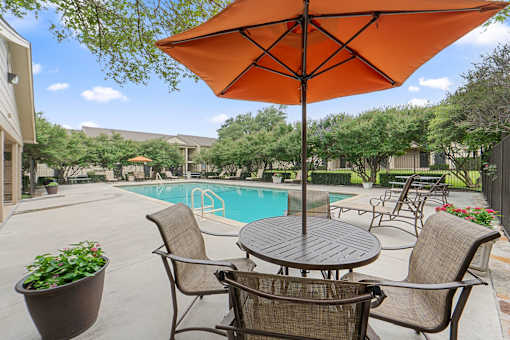 Poolside patio dining with umbrella and seating at Parks on the Green Apartments, Temple, TX 76504