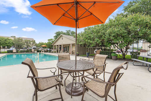 Pool deck with umbrella table and chairs at Parks on the Green Apartments, Temple, TX