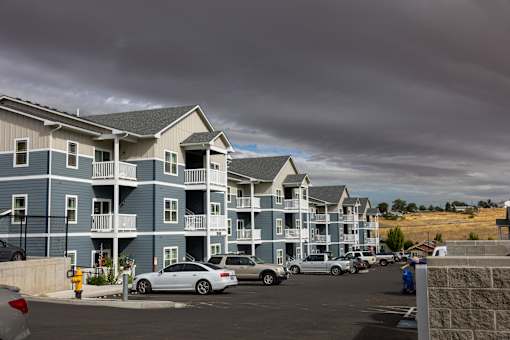 A row of apartment buildings with cars parked in front.