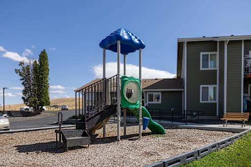 A playground with a blue umbrella and a green slide.