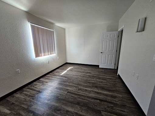 A room with a wooden floor and a window with blinds.