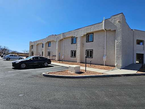 A black car is parked in a parking lot in front of a building.