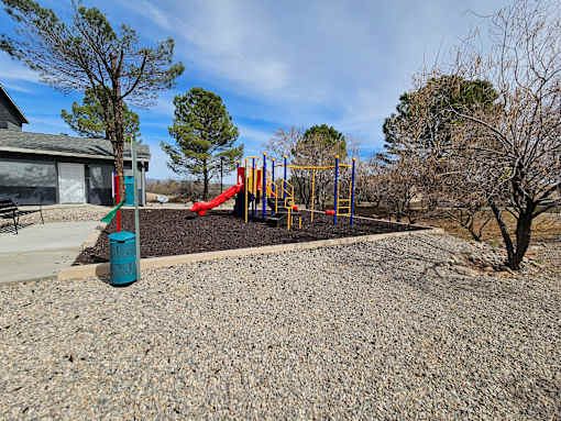 A playground with a slide, swings, and a blue trash can.