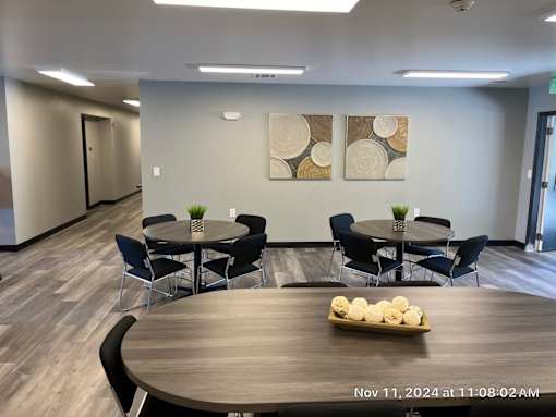 A conference room with a round table and chairs, a vase with flowers, and two abstract paintings on the wall.