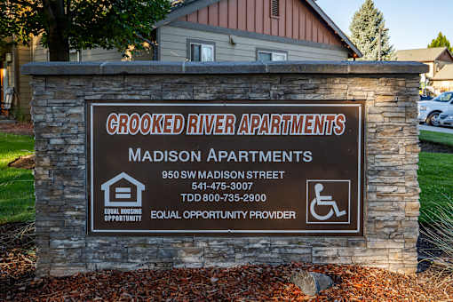 A sign for Crooked River Apartments with a phone number and address.