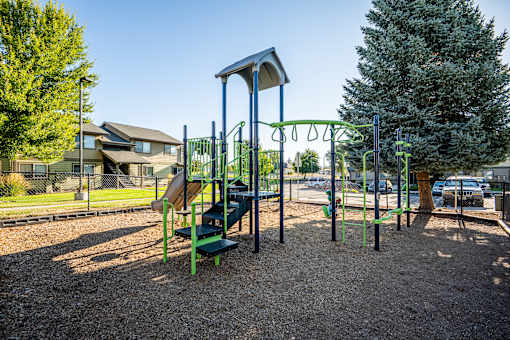 A playground with a green slide and a brown swing set.