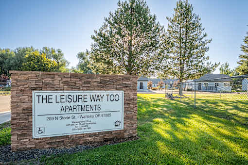 A sign for The Leisure Way Apartments stands in front of a tree.