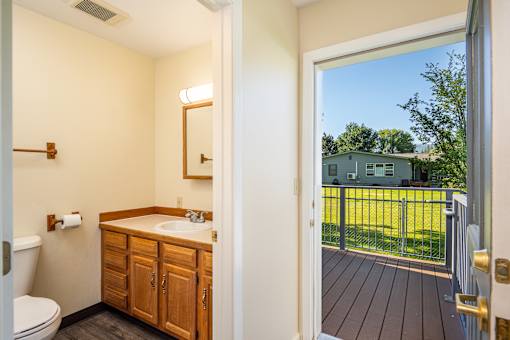 A bathroom with a wooden vanity and a view of a backyard through the door.