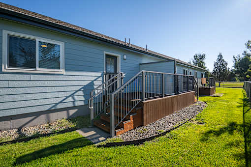 A house with a blue siding and a grey roof with a small porch and a metal railing.