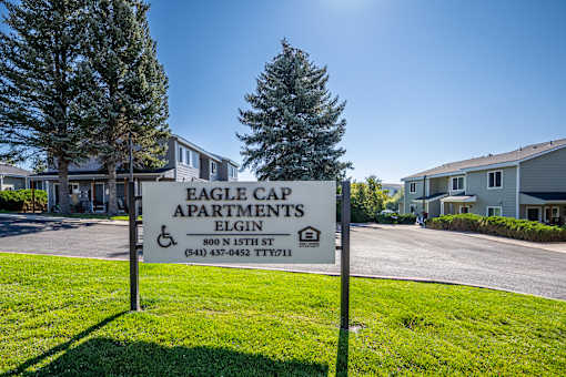 A sign for Eagle Cap Apartments in Elgin stands in front of a building.