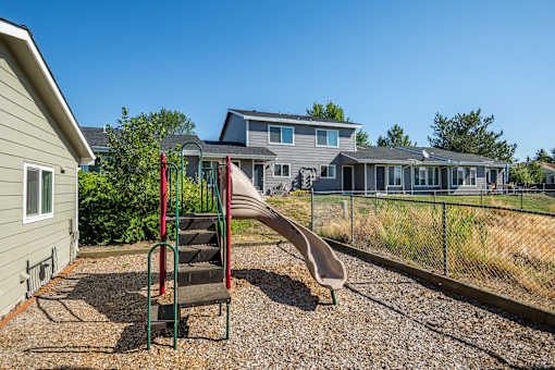 A playground with a slide and a house in the background.