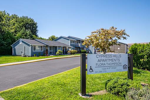 A sign for Cypress Hills Apartments stands in the grass by a road.