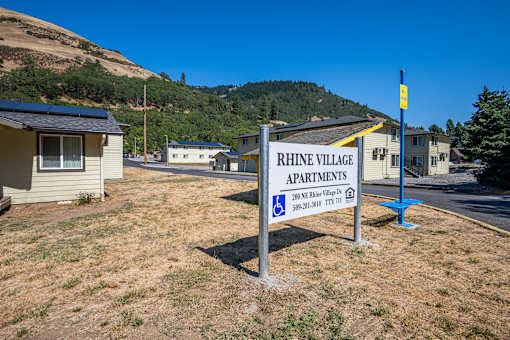 A sign for Rhine Village Apartments stands in a grassy lot.