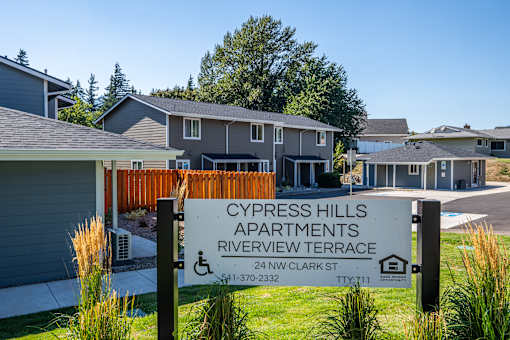 A sign for Cypress Hills Apartments stands in front of a building.