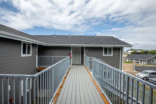 A grey house with a wooden deck and a metal railing.