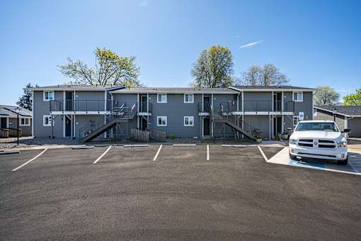 A white truck is parked in a parking lot in front of a grey apartment building.