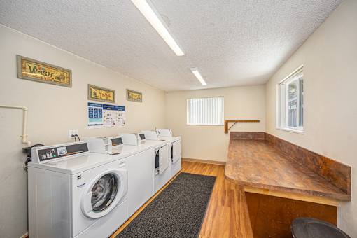 A laundromat with washers and dryers lined up on the left and a bench on the right.