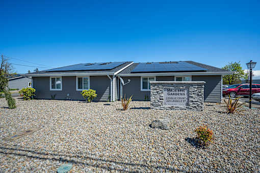 A house with solar panels on the roof and a sign that says "Majestic Gardens".