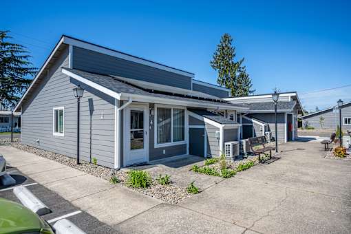 A grey building with a white door and windows is surrounded by a parking lot.