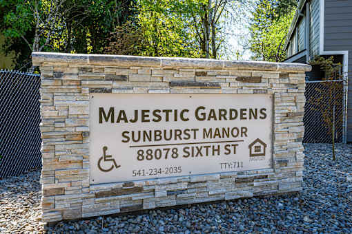 Majestic Gardens Sunburst Manor sign with a stone wall and a fence.