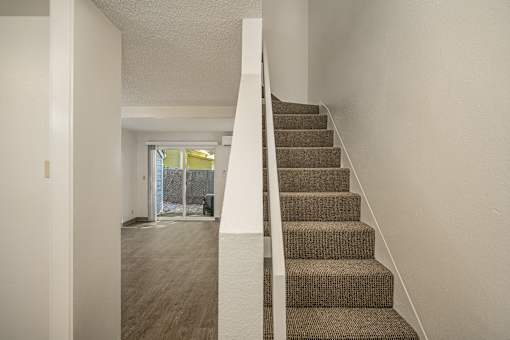A staircase with a carpeted runner and white risers leads to a brightly lit hallway.
