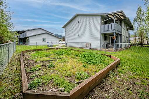 A backyard with a wooden raised garden bed in the foreground and a grey house in the background.