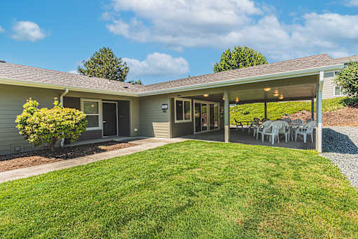 a backyard with a lawn and a patio with tables and chairs