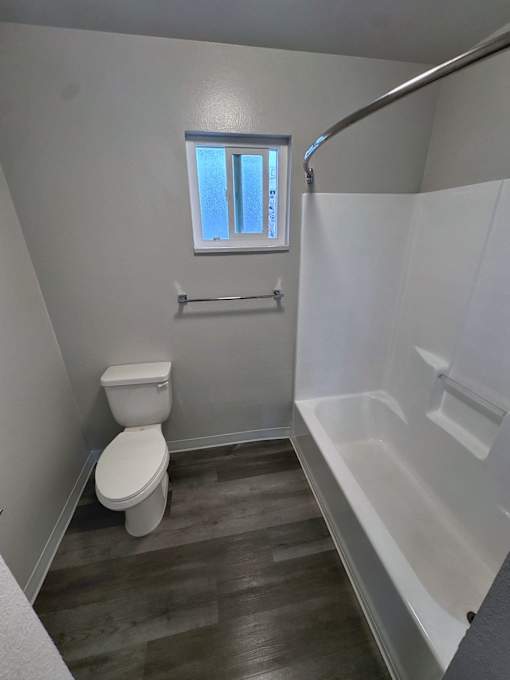 A white toilet sits in a bathroom with a window and a walk-in shower.