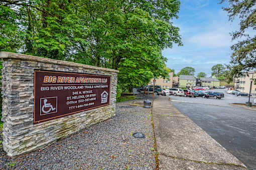 A sign for Big River Apartments stands in front of a parking lot.