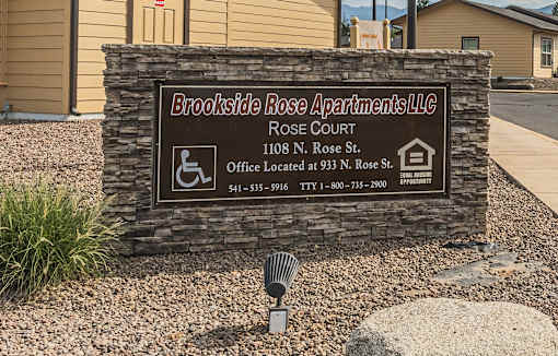 A sign for Brookside Rose Apartments LLC is displayed in front of a building.