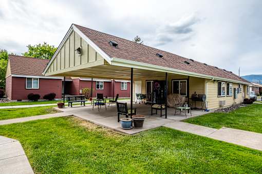 A house with a red and beige exterior has a covered patio with a table and chairs.