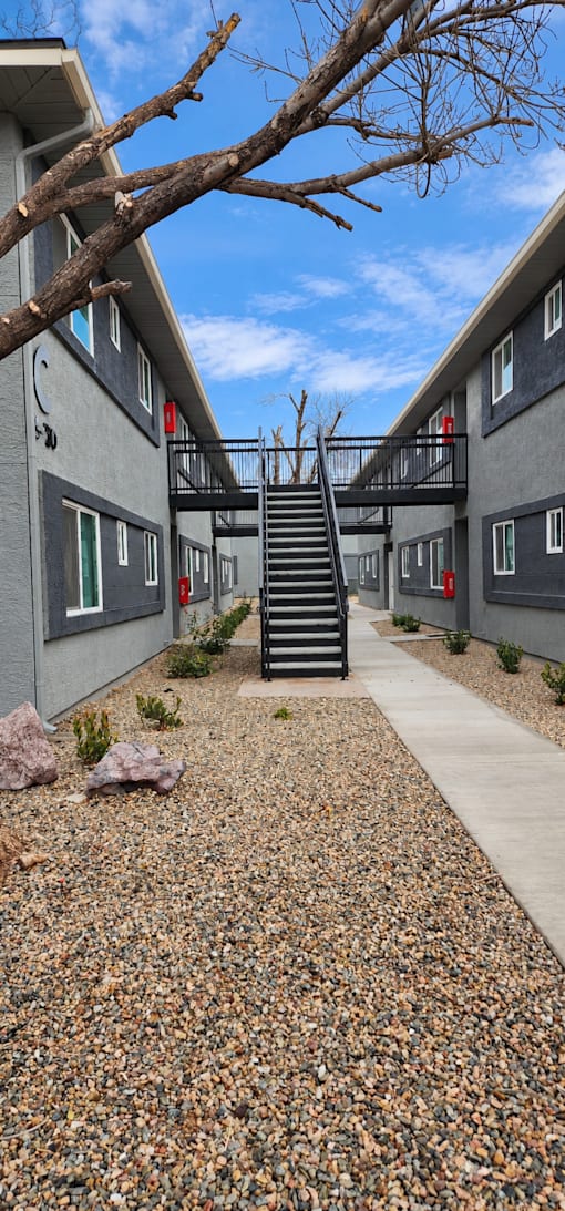 A concrete pathway leads to a black staircase in the middle of a courtyard.