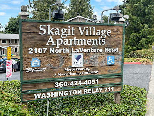 A sign for Skagit Village Apartments with a phone number and a mention of Washington Relay 711.