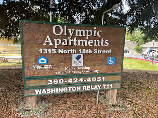 A sign for Olympic Apartments with a phone number and a mention of a housing opportunity.