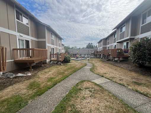 A pathway leads through a grassy area between two rows of apartment buildings.