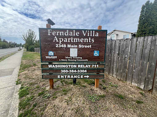 A sign for Ferndale Villa Apartments stands in front of a wooden fence.