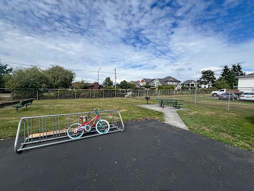 A bike rack with two bikes is in the foreground of a park with a picnic table and a walking path.