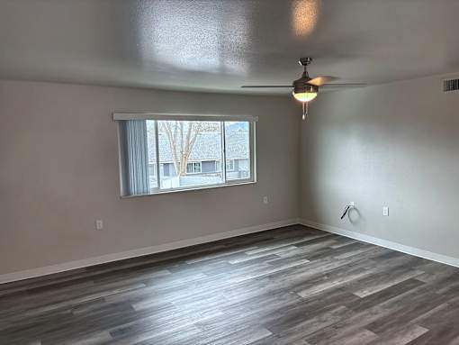 A room with a ceiling fan and a window with a view of a tree and buildings outside.