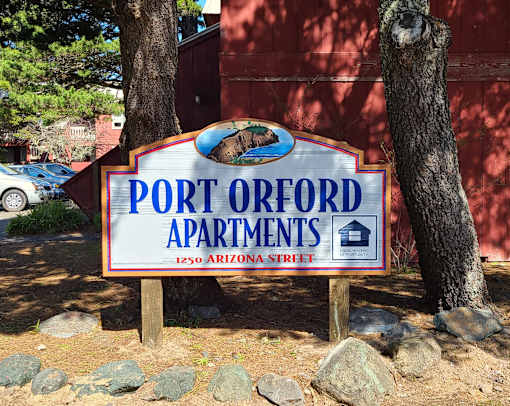 A sign for Port Orford Apartments is displayed in front of a tree.