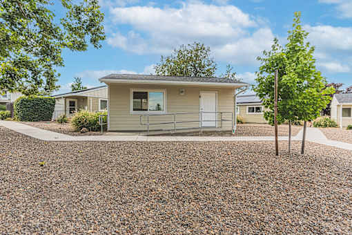 a small tan house with a gravel driveway and trees