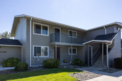 the exterior of a gray house with a balcony and a yard